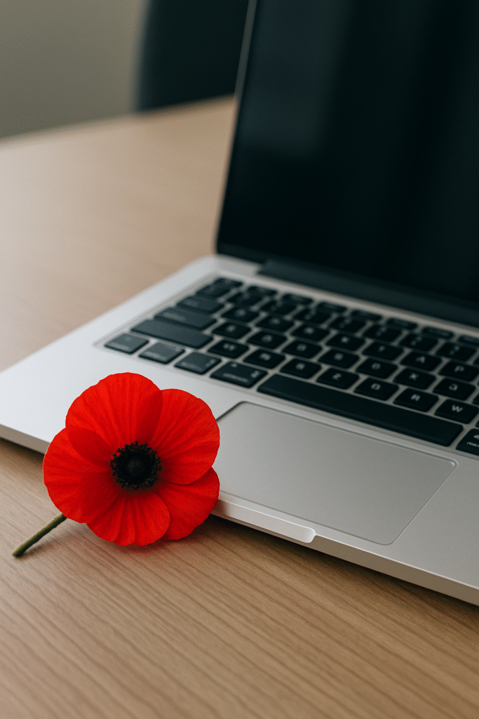 Red remembrance poppy resting beside a laptop on a wooden office desk, representing veteran support and transition into civilian careers.